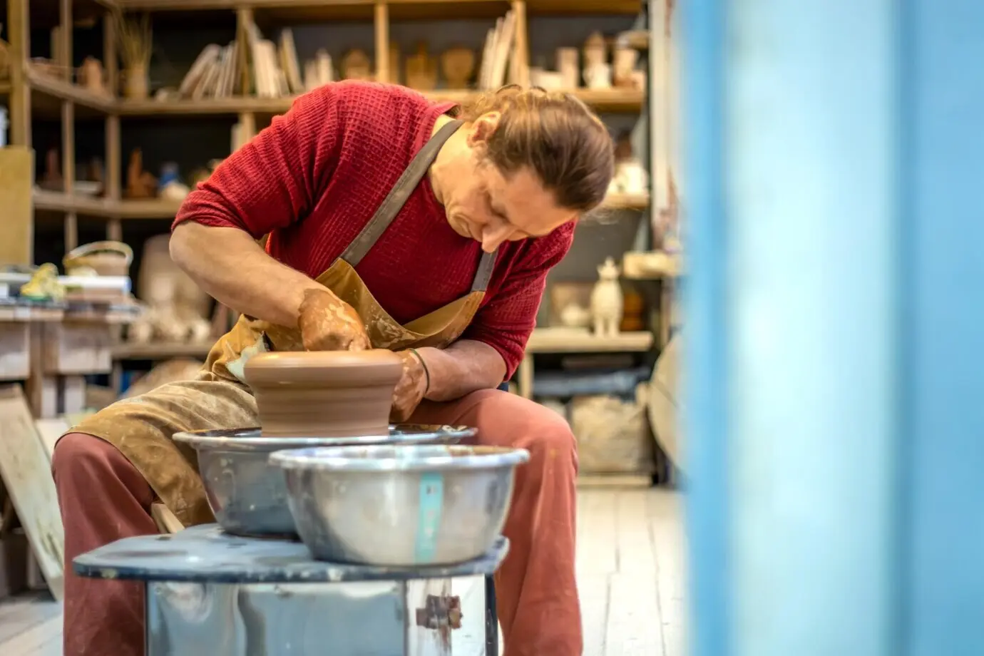 Ein Mann töpfert an einer Töpferscheibe; er stellt Keramik her und modelliert Ton.